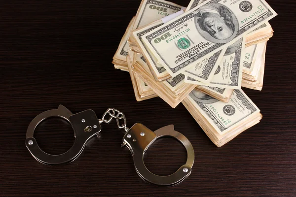 Handcuffs and packs of dollars on wooden table close-up — Stock Photo, Image