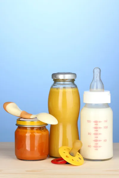 Comida de bebê, garrafa de leite, purê e suco no fundo azul — Fotografia de Stock