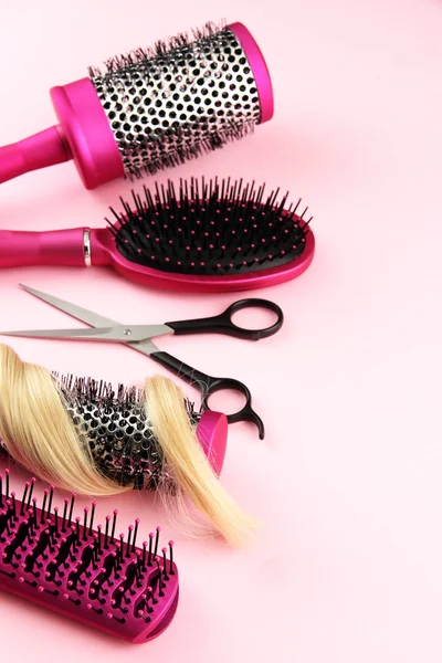 Comb brushes, hair and cutting shears, on pink background — Zdjęcie stockowe