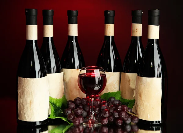 Složení vína lahví, skla a hroznů, na tmavě červeném pozadí — Stock fotografie