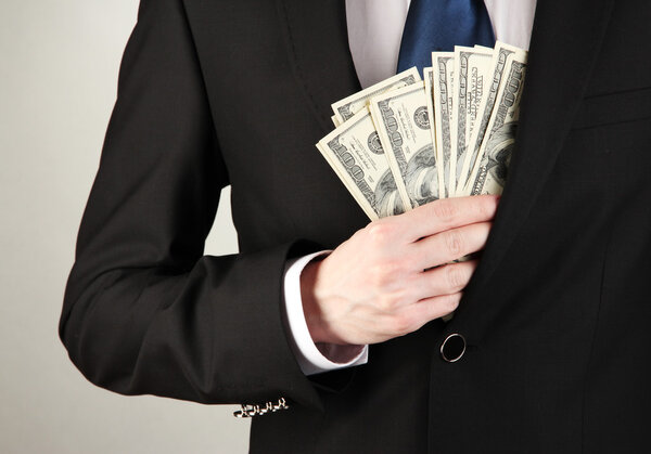 Деловой человек прячет деньги в кармане на сером фоне
