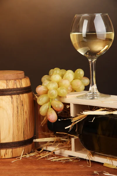 Dřevěné pouzdro s láhev vína, barel, skleničku a hroznů na dřevěný stůl na hnědé pozadí — Stock fotografie