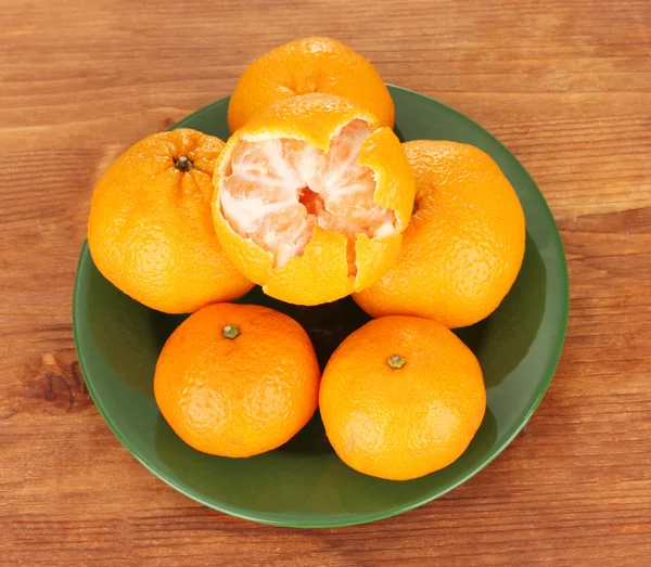 Smakelijke mandarijnen kleur plaat op houten achtergrond — Stockfoto