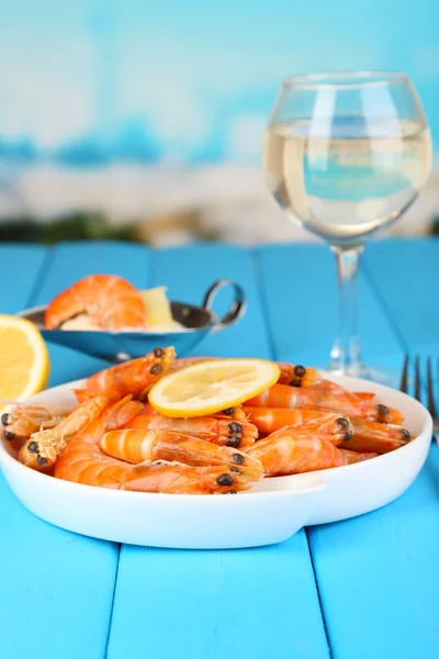 Shrimps with lemon on plate on wooden table on blue natural background — Stock Photo, Image