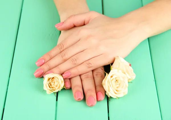 Mãos de mulher com manicure rosa e flores, na cor de fundo de madeira — Fotografia de Stock