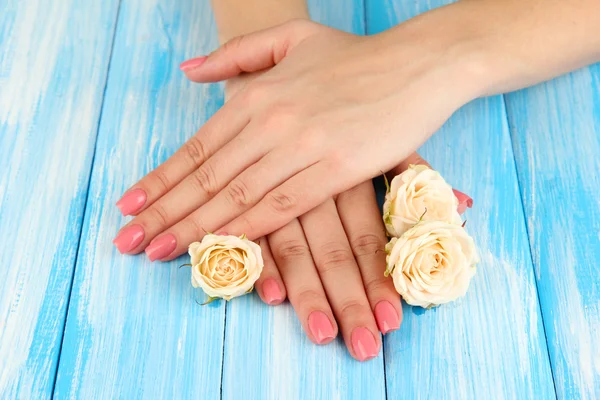 Mãos de mulher com manicure rosa e flores, na cor de fundo de madeira — Fotografia de Stock