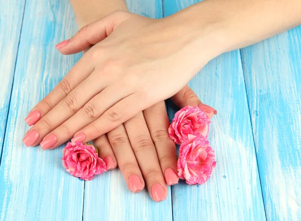 Mãos de mulher com manicure rosa e flores, na cor de fundo de madeira — Fotografia de Stock