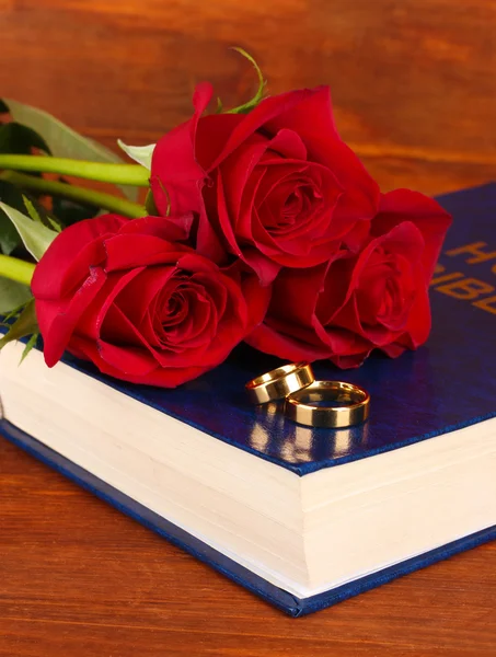 Anillos de boda en la biblia con rosas sobre fondo de madera — Foto de Stock