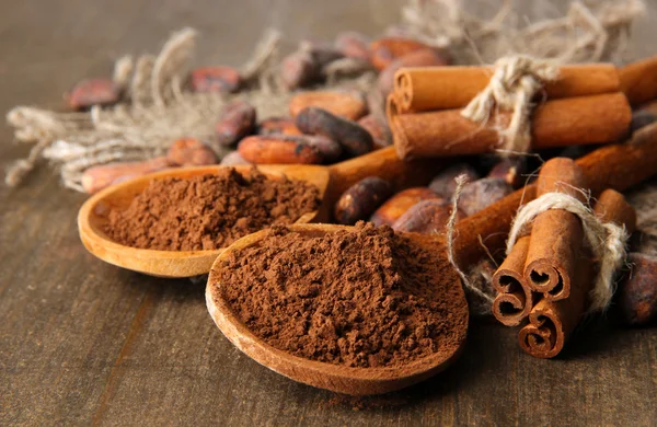 Cacao en polvo en cucharas, granos de cacao y especias sobre fondo de madera — Foto de Stock