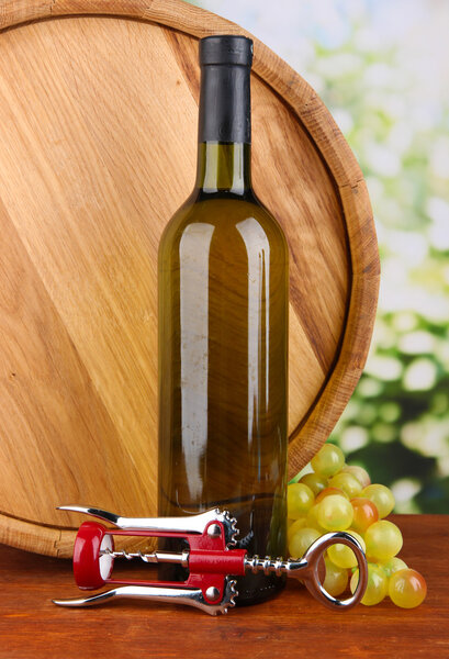 Композиция штопор и бутылка вина, винограда, деревянный бочонок на деревянном столе на ярком фоне

