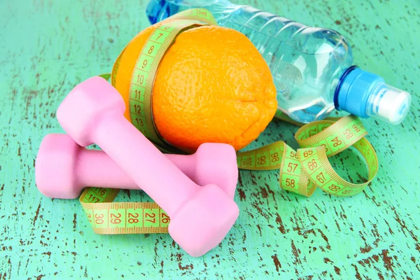 Oranžová s měřicí pásky, činky a láhev vody, na barevné dřevěné pozadí — Stock fotografie