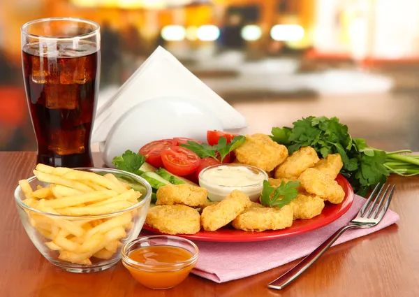 Жареные куриные наггетсы с овощами, колой, картошкой фри и соусом на столе в кафе — стоковое фото