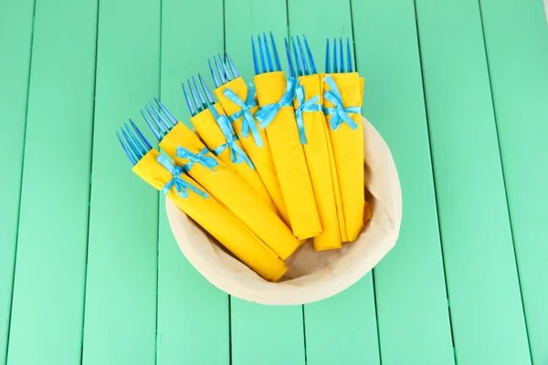Garfos de plástico azul envolto em guardanapos de papel amarelo, em cesta, na cor de fundo de madeira — Fotografia de Stock