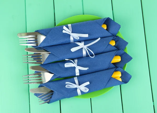 Forks and knives wrapped in blue paper napkins, on color wooden background — Stock Photo, Image