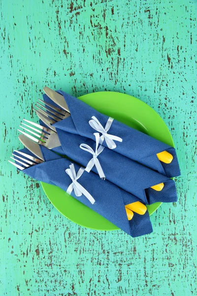 Forks and knives wrapped in blue paper napkin, on color wooden background — Stock Photo, Image