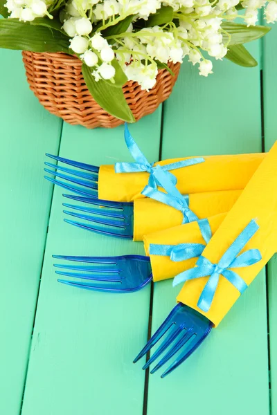 Tenedores de plástico azul envueltos en servilletas de papel amarillo, sobre fondo de madera de color — Foto de Stock