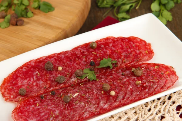 Tasty salami on plate on wooden table close-up — Stock Photo, Image