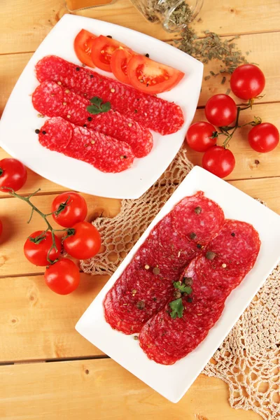 Tasty salami on plates on wooden table close-up — Stock Photo, Image