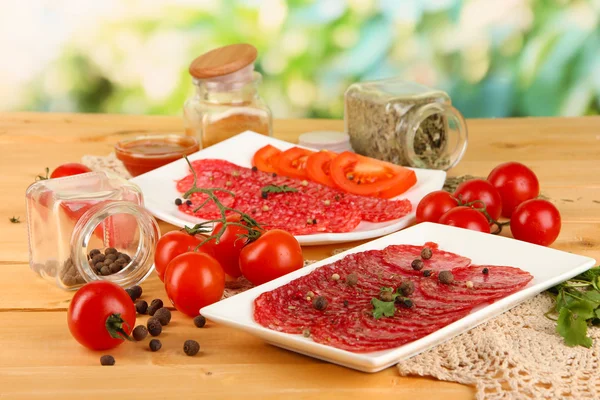 Sabroso salami en platos sobre mesa de madera sobre fondo natural —  Fotos de Stock
