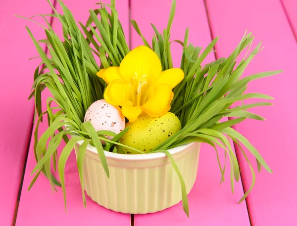 Ovos de Páscoa na tigela com grama na mesa de madeira rosa de perto — Fotografia de Stock