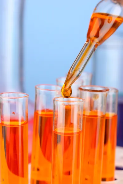 Лабораторная пипетка с каплей цветной жидкости над стеклянными пробирками, крупным планом — стоковое фото