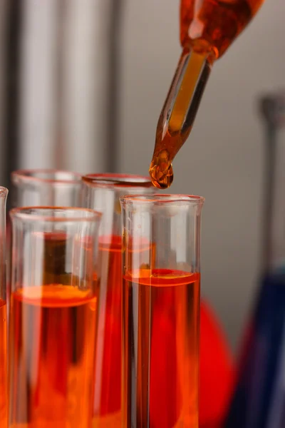 Pipeta de laboratorio con gota de líquido de color sobre tubos de ensayo de vidrio, primer plano — Foto de Stock