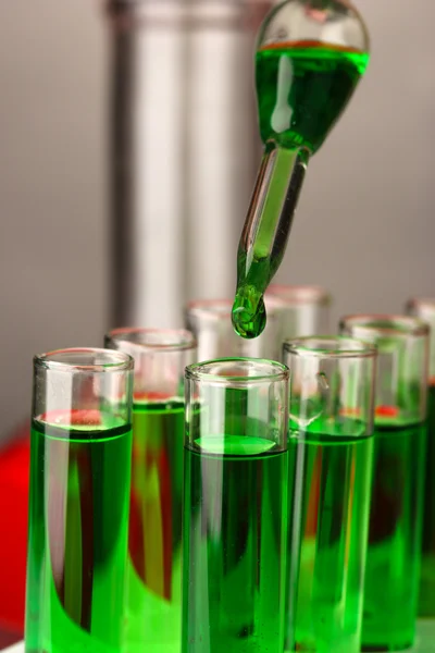 Pipette de laboratoire avec goutte de liquide de couleur sur éprouvettes en verre, gros plan — Photo