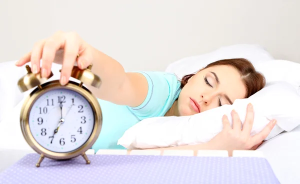 Beautiful young woman sleeping on bed with alarm clock in bedroom — Stock Photo, Image