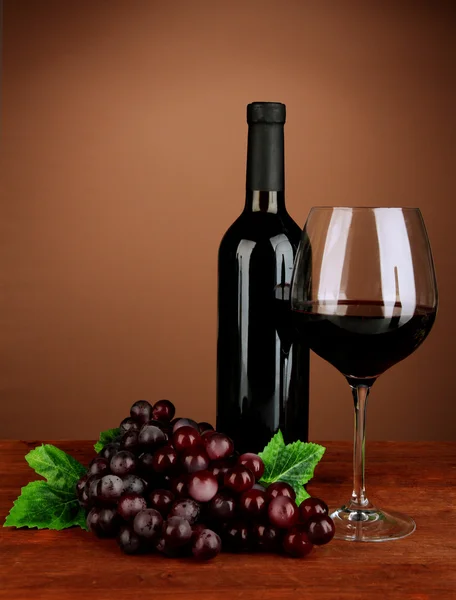 Composition of wine bottle, glass of red wine, grape on color background — Stock Photo, Image
