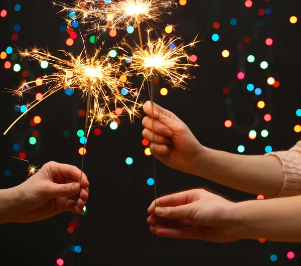 Beautiful sparklers in woman hands on garland backgroun — Stock Photo, Image