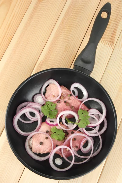 Ein Stück Schweinefleisch mit Zwiebeln in Pfanne auf Holztisch gebraten — Stockfoto