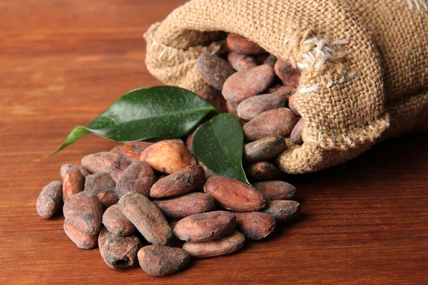 Какао-бобы в мешке с листьями на деревянном фоне — стоковое фото