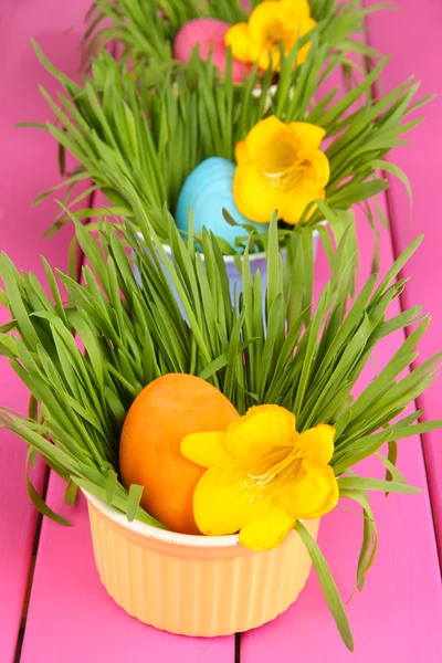 Easter eggs in bowls with grass on pink wooden table close up — Stock Photo, Image