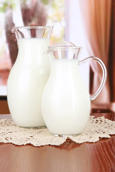 Pitchers of milk on table in room — Stock Photo, Image