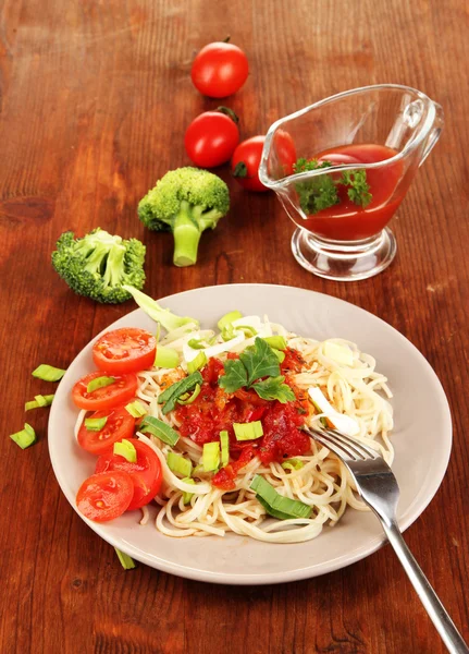 Espaguete saboroso com molho e legumes na placa na mesa de madeira close-up — Fotografia de Stock