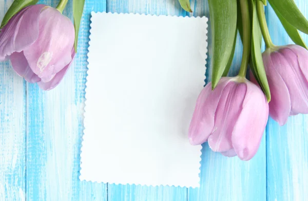 Hermoso ramo de tulipanes morados y tarjeta en blanco sobre fondo de madera azul —  Fotos de Stock