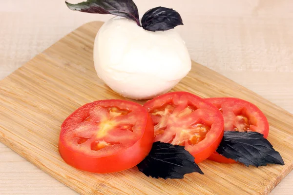 Smakelijke mozzarella met tomaten op het bord hakken op mat — Stockfoto