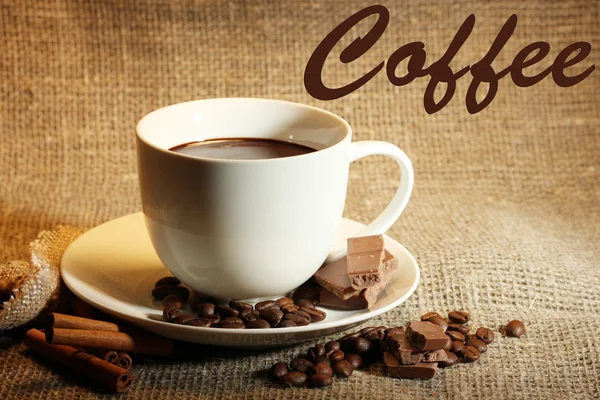 Kopje koffie en bonen, kaneelstokjes en chocolade op rouwgewaad achtergrond — Stockfoto