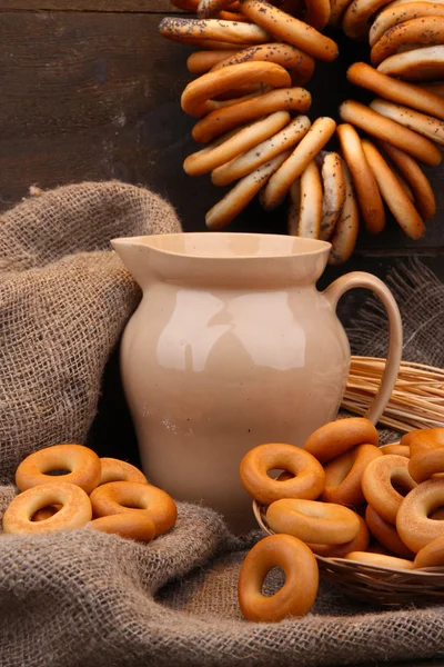 罐牛奶、 美味的面包圈和小穗木制背景上 — 图库照片