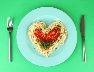 dikkatli bir şekilde kalp şeklinde düzenlenmiş ve renkli arka plan üzerinde domates soslu tepesinde pişmiş spagetti