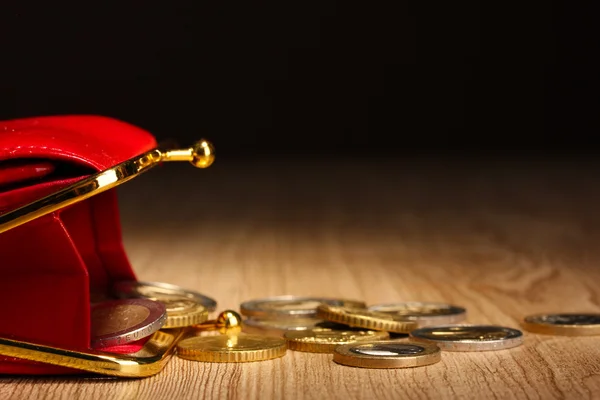 Billetera roja femenina con monedas sobre mesa de madera, sobre fondo negro — Foto de Stock