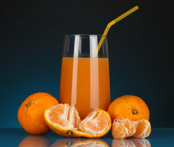 Utsökt tangerine juice i glas och mandariner bredvid den på Mörkblå bakgrund — Stockfoto