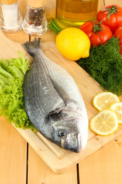 Dorado fresco em tábua de cortar com limão e legumes em mesa de madeira — Fotografia de Stock