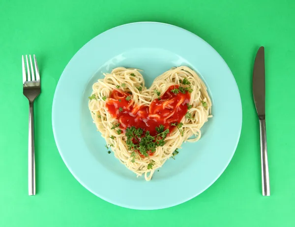 Cooked spaghetti carefully arranged in heart shape and topped with tomato sauce, on color background — Stock Photo, Image