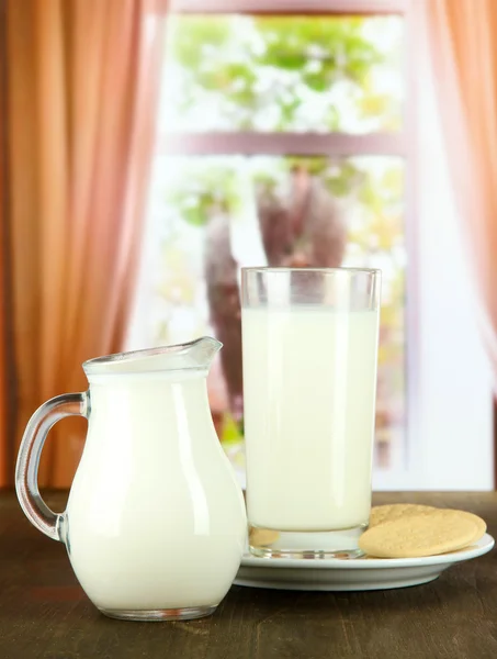 Стакан молока, кувшин и печенье на фоне комнаты — стоковое фото