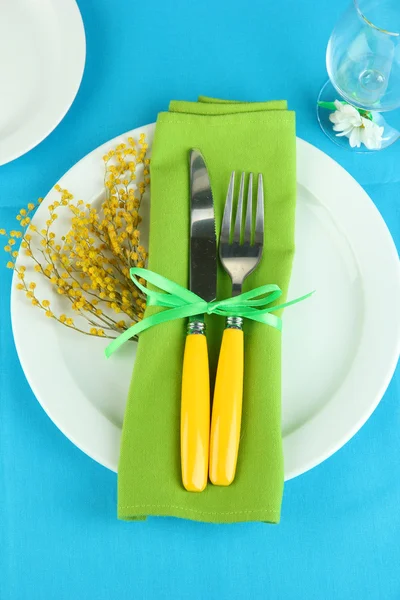 Knife and fork wrapped in napkin, on plate, on color tablecloth background — Stock Photo, Image