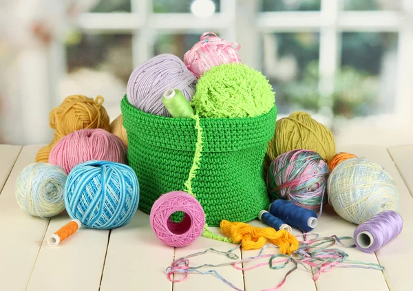 Colorful yarn for knitting in green basket on wooden table on window background — Stock Photo, Image