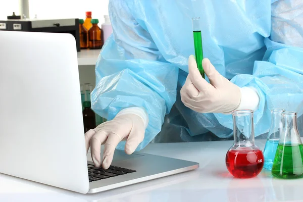 Scientist entering data on laptop computer with test tube close up — Stock Photo, Image