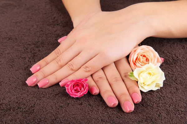 Kobieta ręce z różowy manicure i kwiaty, na kolor tła — Zdjęcie stockowe