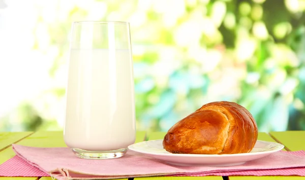 面包卷和一杯牛奶在明亮的背景上的木桌上 — 图库照片